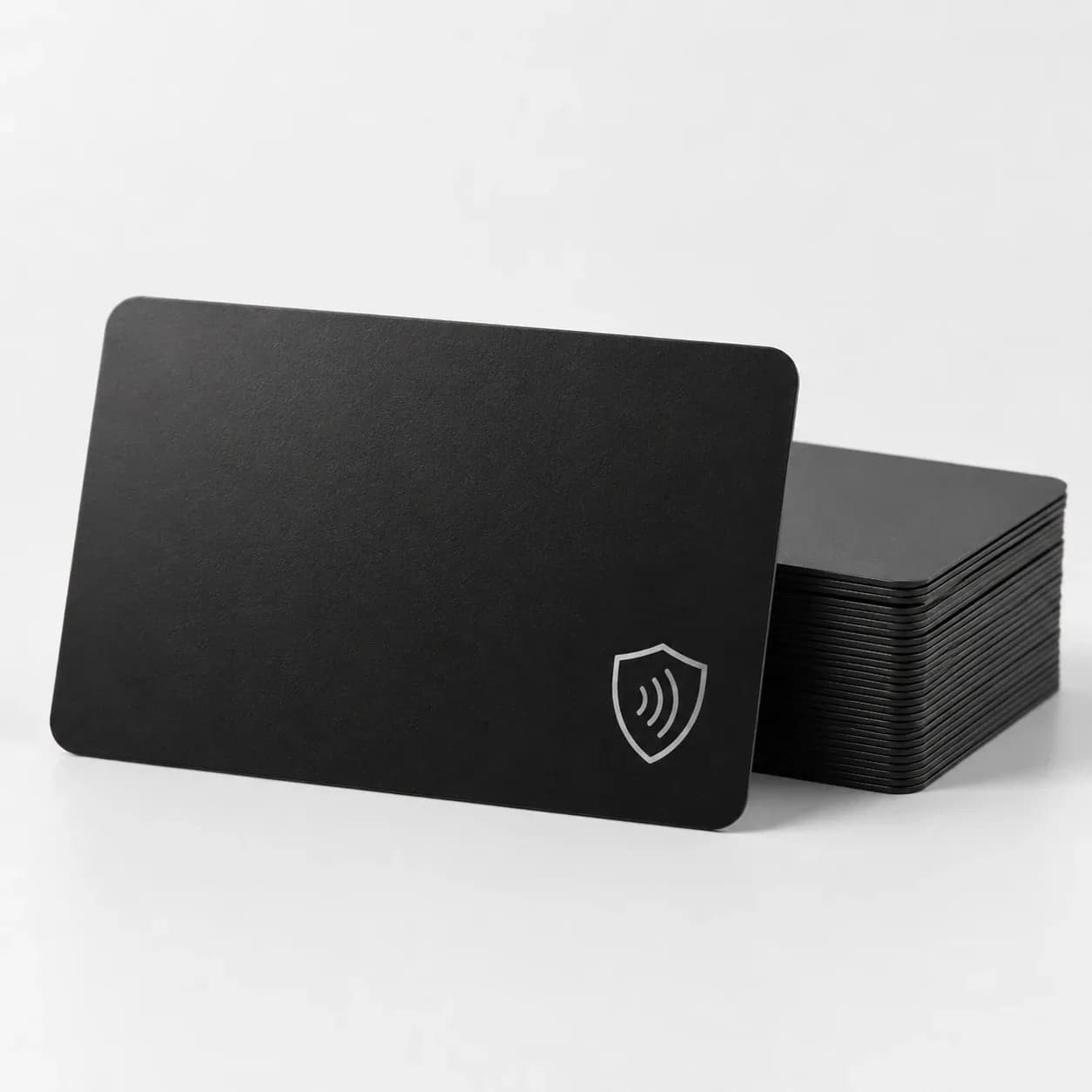 Black RFID blocking card with a silver shield and contactless symbol, in front of a stack